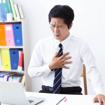 A teacher at his desk grasps his chest in pain